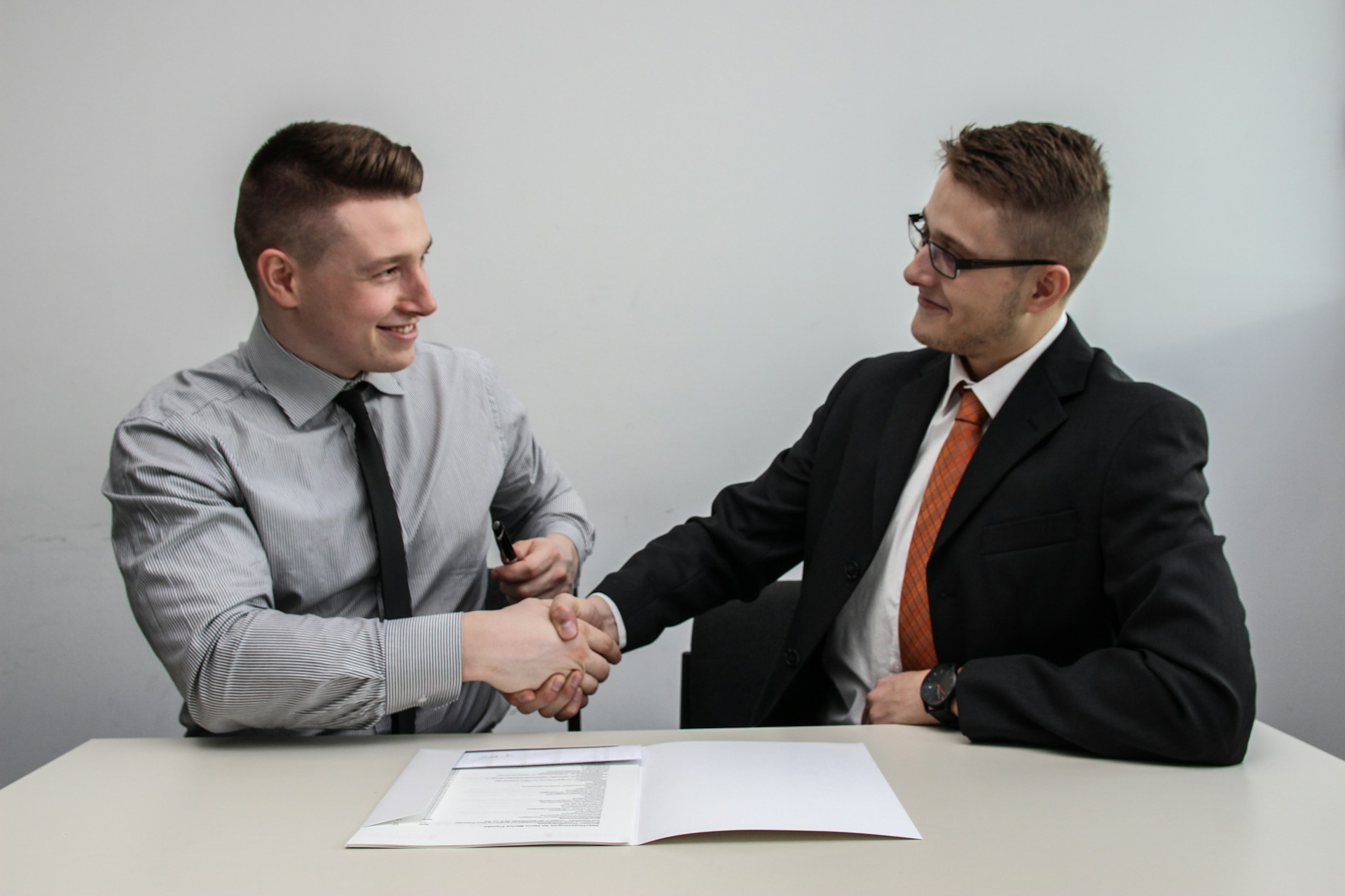 two men sitting at a table shacking hands